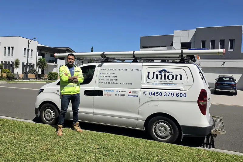 Union Air Conditioning technician in a hi-vis jacket with the Union logo, standing beside the white Union van parked on a Sydney street